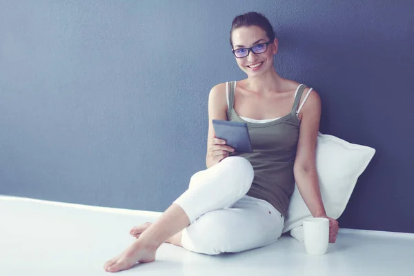 Krásná mladá žena s šálkem čaje, zatímco sedí na podlaze doma pomocí tabletového počítače — Stock fotografie