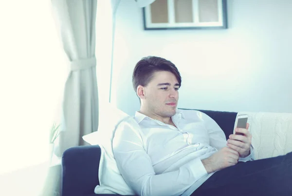 Hezký muž sedí pohovka pomocí smartphone doma — Stock fotografie