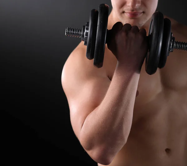 Cara muscular fazendo exercícios com halteres sobre fundo escuro — Fotografia de Stock