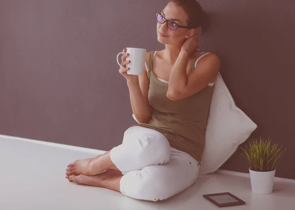 Una hermosa joven sana sentada en el suelo con una taza de té o café sonriendo. aislado sobre fondo blanco — Foto de Stock