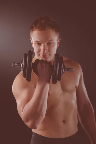 Muscular guy doing exercises with dumbbells over dark background — Stock Photo, Image