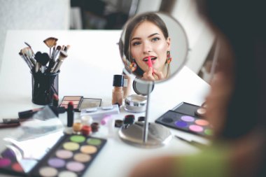 Genç ve güzel bir kadın aynanın yanında makyaj yapıyor.