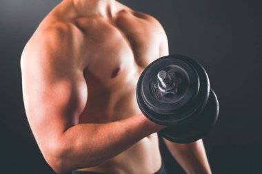 Karanlık duvarda stil sahibi üstsüz bir adam.