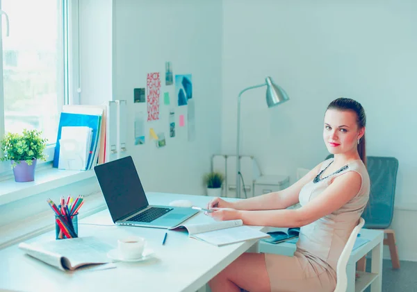 Jolie femme assise au bureau, travaillant avec un ordinateur portable, tenant un document — Photo