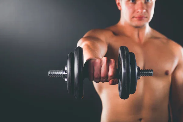 Musculoso chico haciendo ejercicios con mancuernas sobre fondo oscuro — Foto de Stock