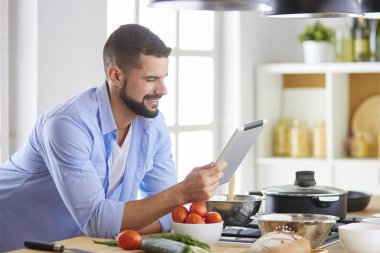 Dijital tablet ve yemek pişirme tarifine uyan bir adam evdeki mutfakta lezzetli ve sağlıklı yemekler pişiriyor.