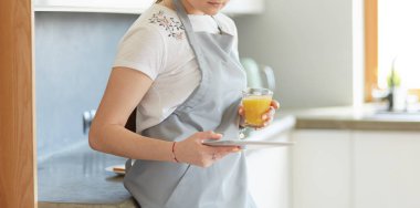 Mutfakta portakal suyu ve tableti olan genç bir kadın.