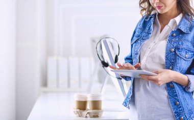Gülümseyen kadın kahve içiyor ve kafede tablet kullanıyor.