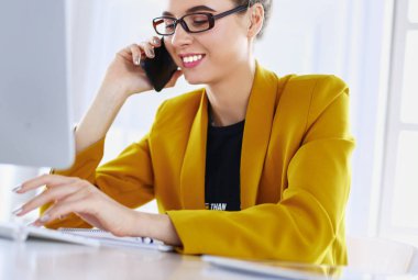İş kadını ofiste bilgisayar ve cep telefonu kullanarak işine konsantre oluyor.