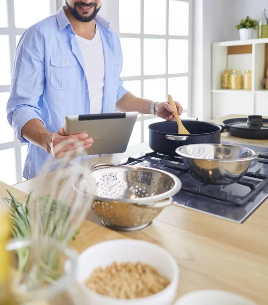 Man following recipe on digital tablet and cooking tasty and healthy food in kitchen at home — Stock Photo, Image