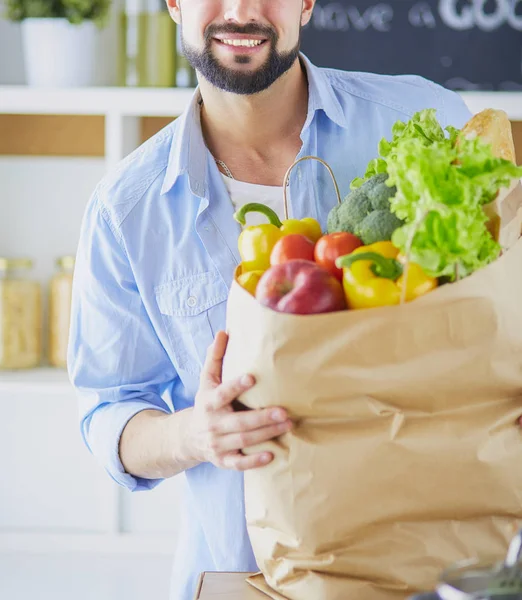 Man holding paper bag full of groceries on the kitchen background. Shopping and healthy food concept