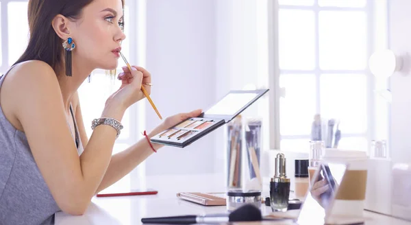 Mujer morena aplicando maquillaje para una cita nocturna frente a un espejo — Foto de Stock