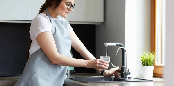 Menselijke hand holding glas gieten vers drinkwater bij keukenkraan — Stockfoto