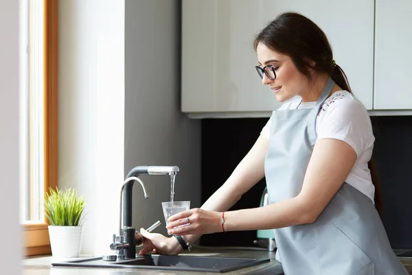 Menselijke hand holding glas gieten vers drinkwater bij keukenkraan — Stockfoto