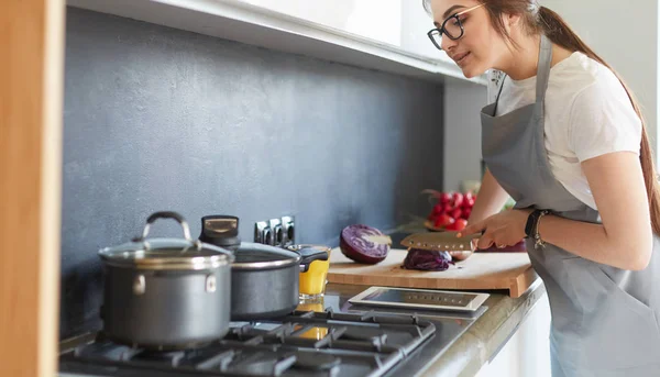 Ung kvinna använder en surfplatta dator för att laga mat i sitt kök — Stockfoto