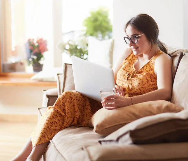 Mladá žena, která sedí na gauči a pracuje na přenosném počítači doma — Stock fotografie