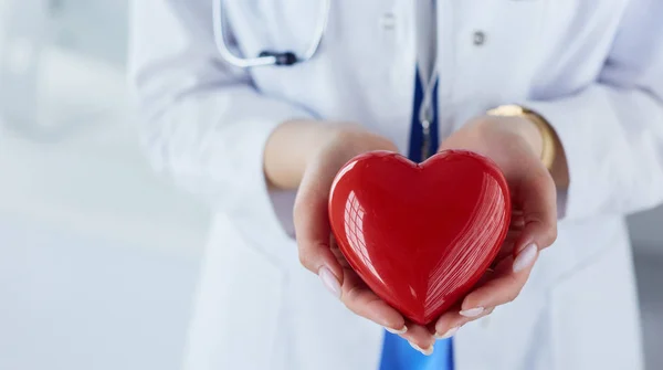 Female doctor with stethoscope holding heart, on light background — Stock Photo, Image