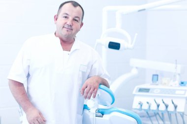 Diş kliniğinde duran gülümseyen bir dişçinin portresi.