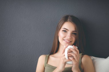 Bir fincan çay ya da kahveyle yerde oturmuş gülümseyen sağlıklı bir genç.