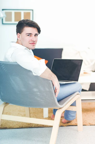 Genç adam sandalyede oturuyor ve dizüstü bilgisayarla çalışıyor. — Stok fotoğraf