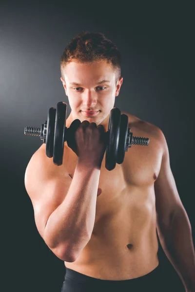 Musculoso chico haciendo ejercicios con mancuernas sobre fondo oscuro — Foto de Stock