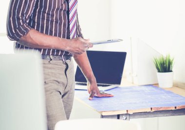 Ofiste bilgisayar ve planlarla çalışan Afrikalı Amerikalı bir mimar.