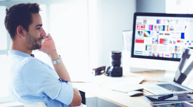 İnternette çalışırken bilgisayarın ve dizüstü bilgisayarın önünde grafik stüdyosunda oturan genç tasarımcının portresi.