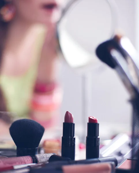 Joven hermosa mujer haciendo maquillaje cerca del espejo, sentado en el escritorio — Foto de Stock