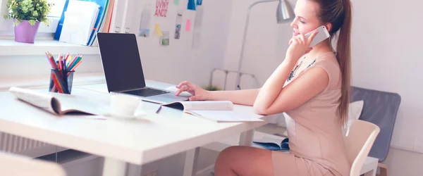 Jovem empresária sentada na mesa e conversando ao telefone — Fotografia de Stock