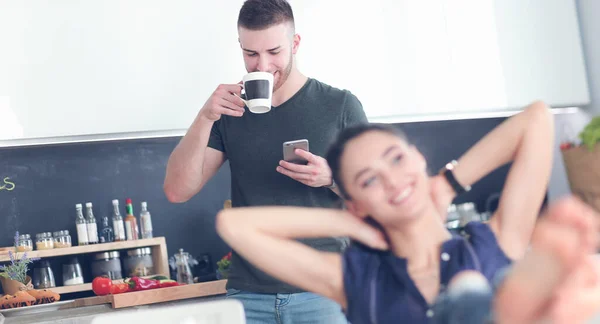 Pareja feliz usando smartphone sentado en la cocina —  Fotos de Stock