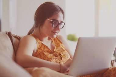 Evde dizüstü bilgisayar üzerinde çalışan kanepede oturan genç kadın