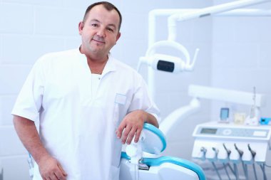 Diş kliniğinde duran gülümseyen bir dişçinin portresi.