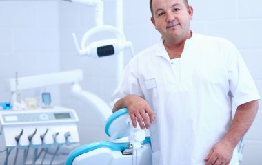 Diş kliniğinde duran gülümseyen bir dişçinin portresi.