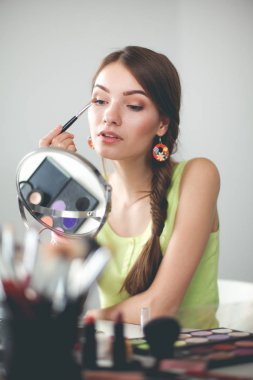 Genç ve güzel bir kadın aynanın yanında makyaj yapıyor.