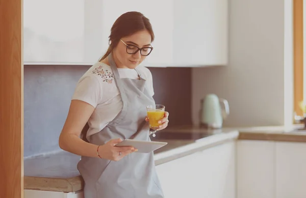 Mujer joven con jugo de naranja y tableta en la cocina — Foto de Stock