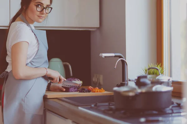 Mujer joven cortando verduras en la cocina de pie cerca del escritorio — Foto de Stock