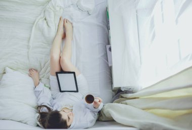 Sabahları yatakta otururken tablet kullanan ve kahve içen kadın portresi