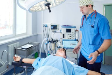 Ameliyat odasında arka planda erkek cerrah var.