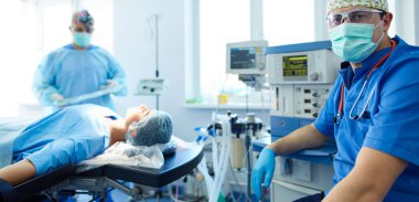 Ameliyat odasında arka planda erkek cerrah var.