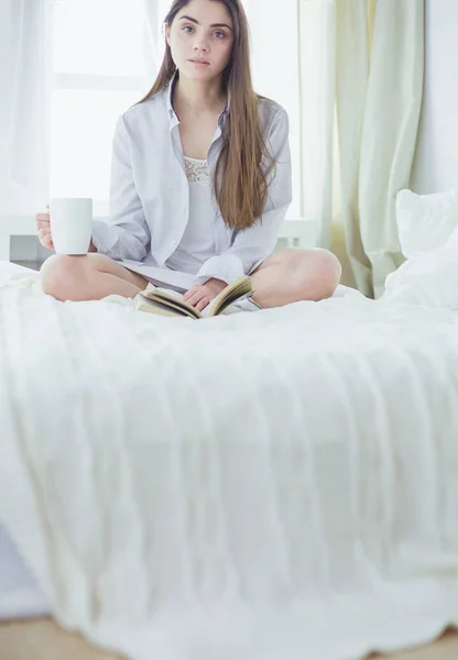 Γυναίκα που κάθεται στο κρεβάτι διαβάζοντας ένα βιβλίο και τρώγοντας πρωινό — Φωτογραφία Αρχείου