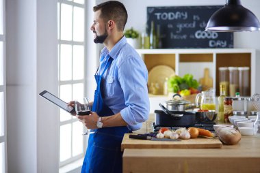Dijital tablet ve yemek pişirme tarifine uyan bir adam evdeki mutfakta lezzetli ve sağlıklı yemekler pişiriyor.