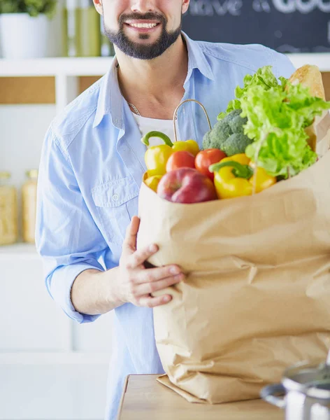 Hombre sosteniendo bolsa de papel llena de comestibles en el fondo de la cocina. Compras y concepto de comida saludable — Foto de Stock