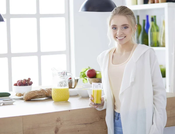 Attractive woman holding a glass of orange juice while standing in the kitchen — Stock Photo, Image