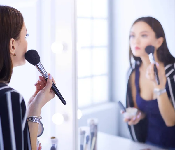 Красивая девушка смотрит в зеркало и наносит косметику большой кистью — стоковое фото