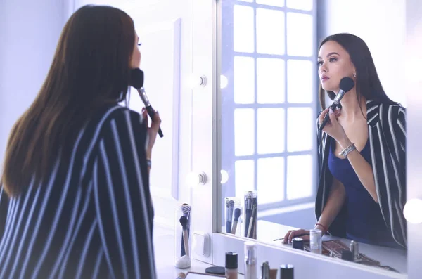 Skönhet kvinna tillämpa makeup. Vacker flicka ser i spegeln och tillämpa kosmetiska med en stor pensel — Stockfoto