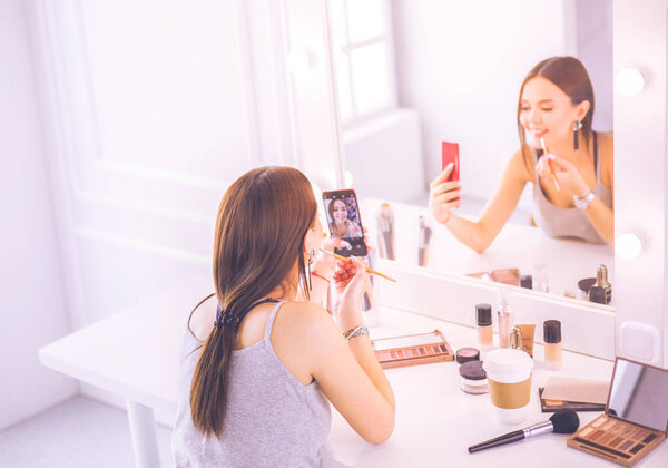 Beauty blogger filming makeup tutorial with smartphone in front of mirror