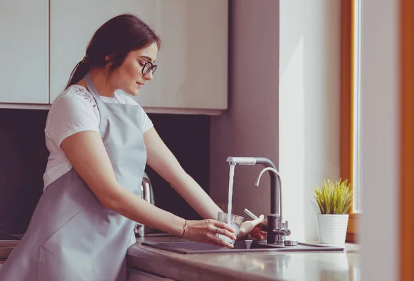 Рука людини тримає скло, наливаючи свіжу питну воду на кухонний кран — стокове фото