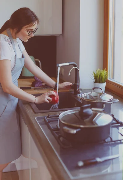 Mujer lavando verduras. Hermosa joven lavando verduras para ensalada y sonriendo mientras está de pie en la cocina — Foto de Stock