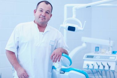 Diş kliniğinde duran gülümseyen bir dişçinin portresi.