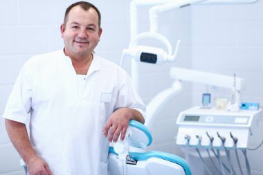 Diş kliniğinde duran gülümseyen bir dişçinin portresi.
